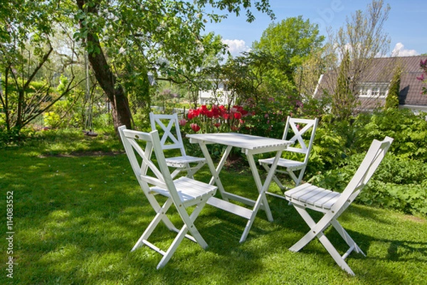 Fototapeta white wooden table and chairs standing on a lawn at the garden