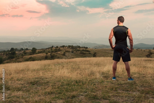 Fototapeta Athletic man in his 30s resting with his hands on his hips while jogging outdoor