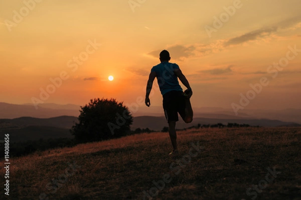 Fototapeta Silhouette of an athletic man in nature in front of a sunset while exercising