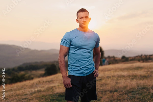 Fototapeta Athletic man in his 30s resting with his hands on his hips while jogging outdoor