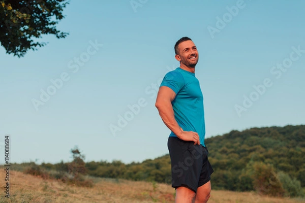 Fototapeta Athletic man in his 30s resting with his hands on his hips while jogging outdoor