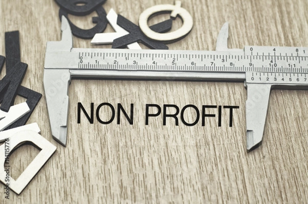Fototapeta Business motivation and finance concept, vernier caliper with word NON PROFIT over wooden floor and alphabetical word made from wood background