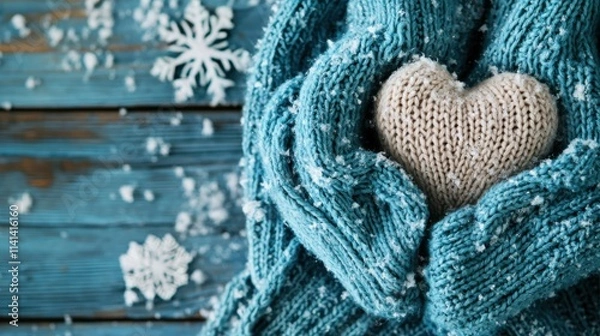 Fototapeta A cozy knit scarf cradles a soft heart-shaped object, surrounded by snowflakes on a rustic wooden background, evoking warmth in winter.