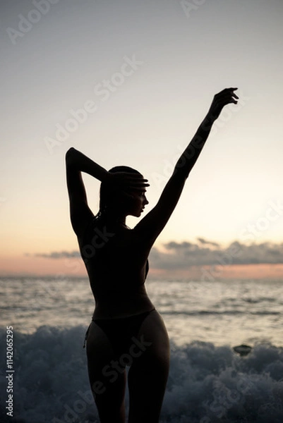 Obraz A beautiful silhouette of a woman enjoying the serene sunset at a peaceful beach
