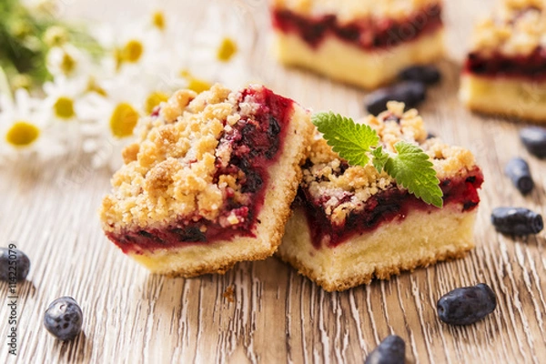 Fototapeta Honeysuckle Crumb Cake  sliced into pieces on a light background with berries of honeysuckle and flowers 