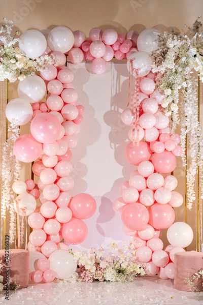 Fototapeta Photo zone for wedding receptions, or festive zone for celebrating girl's birthday party. Arch decorated with pink and white balloons, flowers. Photo wall decoration space or place for text.