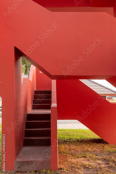 Fototapeta A vibrant red architectural structure, angular walls and a set of stairs leading upwards