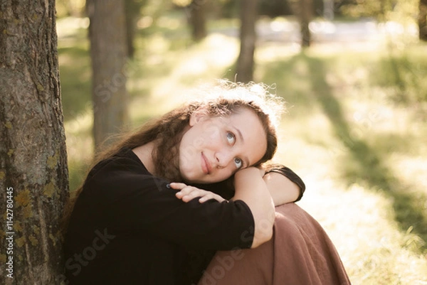 Fototapeta Girl in nature in the park. Curly girl in a linen dress. Sunny day and beautiful sunlight. Warm photos of a girl enjoying nature in a good mood. Walking alone with yourself and the beauty of nature.