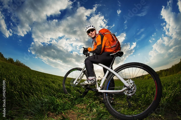 Fototapeta Young man riding on bicycle through deep grass with backpack