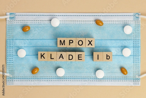 Fototapeta Mpox Klade Ib (Clade in German) is laid out with wooden cubes on a surgical face mask, surrounded by various pills. MPOX is the new name for the monkeypox virus.