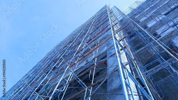 Fototapeta Scaffolding next to a new building. Building under construction with metal scaffolding set beside a commercial or residential building on a crane and sky background with copy space and selective focus