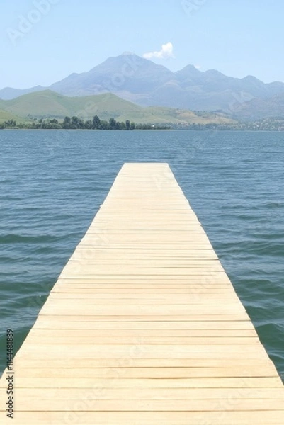 Fototapeta Wooden dock extending over calm lake towards distant mountains under a clear sky.