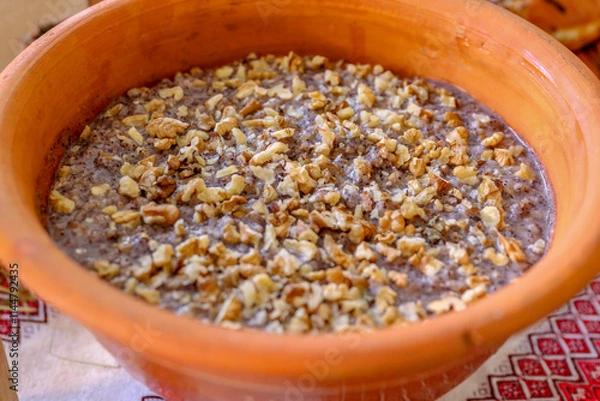 Fototapeta Clay bowl with traditional Ukrainian kutya sprinkled with chopped nuts. The background of the photo is made in folk style with the use of embroidery.