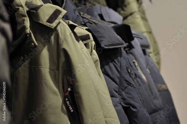 Fototapeta Colorful Jackets and Coats Neatly Hung on a Rack in a Fashion Store. Concept of Winter Apparel, Textile Variety, Retail Display, clothes shop, and Clothing Organization.
