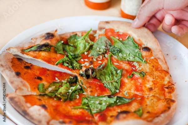 Fototapeta Taking slice of hot pizza. Tasty pizza with with cheese and greens, closeup view. 