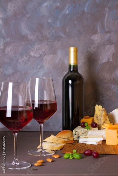 Fototapeta Glasses and bottle of red wine and wine appetizers cheese, bread and nuts on brown wooden background with copy space