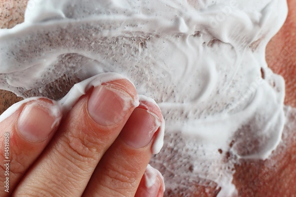 Fototapeta Hand puts shaving foam on cheek close up