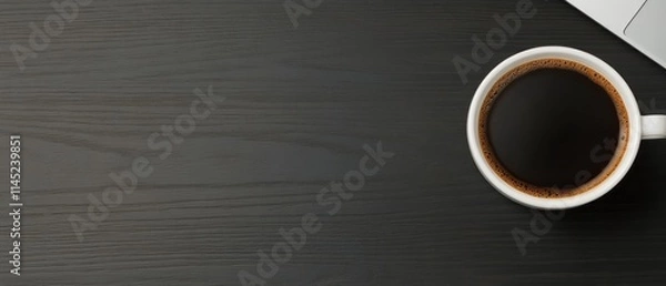 Obraz Hot black coffee rests on a dark wooden table next to a notebook for easy access during work
