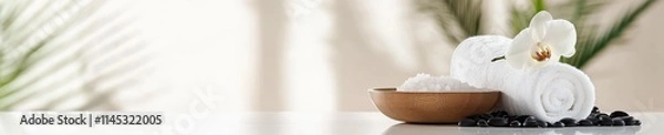 Fototapeta Neatly arranged spa essentials feature a soft towel roll a wooden bowl of salts black pebbles and an elegant orchid. This tranquil setup promotes relaxation and wellness in a bright environment