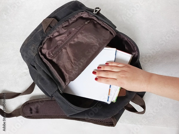Fototapeta A hand puts textbooks in a school bag. Books from the library. Exam, test. The beginning and the end of the school year. Educational materials. Workload during studies.