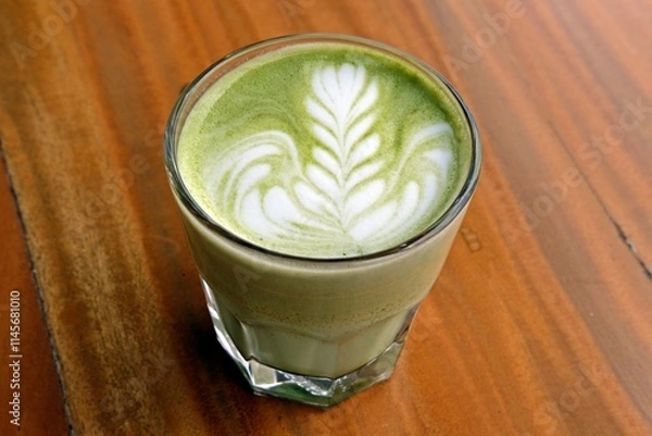 Obraz A beautifully crafted matcha latte in a clear glass, with delicate latte art on top. This creamy green tea beverage is a perfect blend of earthy matcha flavor and smooth, frothy milk,
