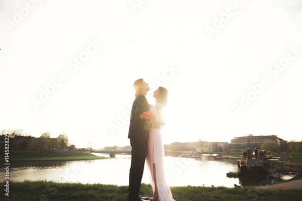 Fototapeta Elegant beautiful wedding couple posing near river at sunset
