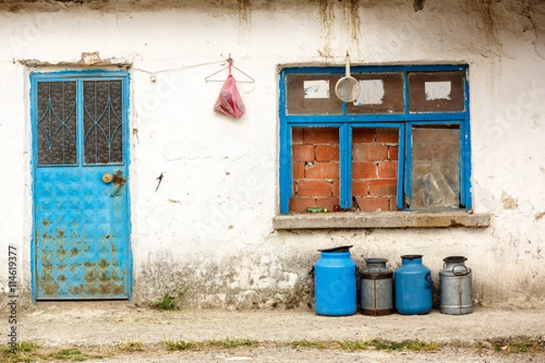 Obraz old milk jugs in a row in front of an abandoned house