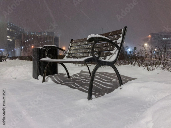 Fototapeta Cast iron bench standing in the park during snowfall.