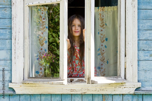 Obraz Happy little girl opens a window of rustic house in the early sunny morning