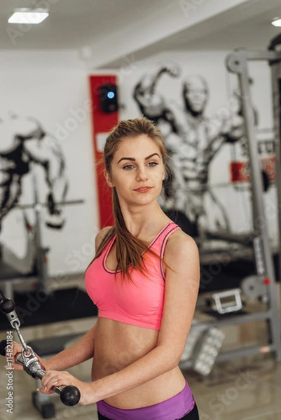 Fototapeta Blonde performs an exercise on the simulator