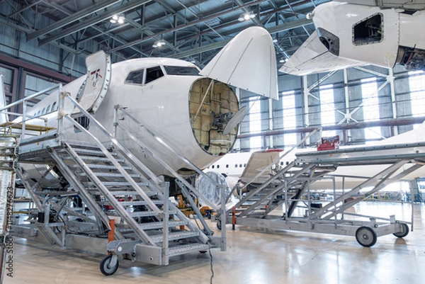Obraz Front view of the white passenger plane under maintenance in the airplane hangar. The aircraft has opened weather radar. Checking mechanical systems for flight operations