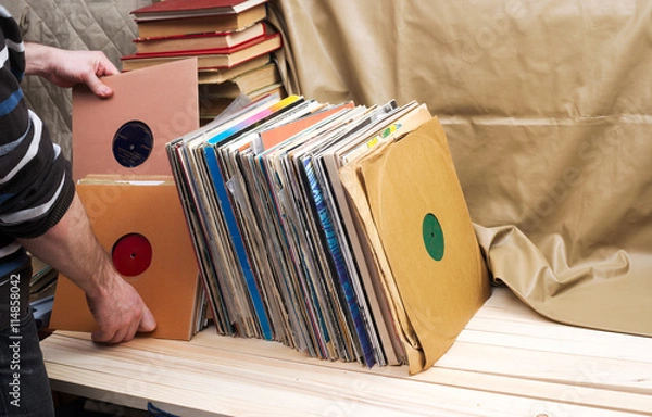 Fototapeta Retro styled image of a collection of old vinyl record lp's with sleeves on a wooden background. Browsing through vinyl records collection. Music background. Copy space