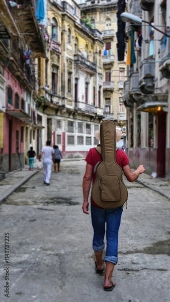 Fototapeta A boy with a guitar on his back walks the streets of Havana 
