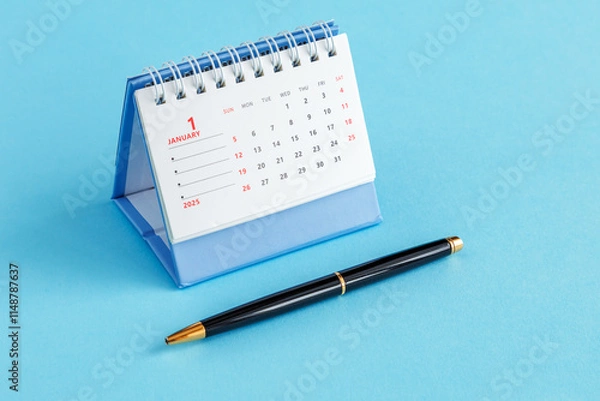 Fototapeta A desktop calendar for 2025 and a black ballpoint pen on a blue background.