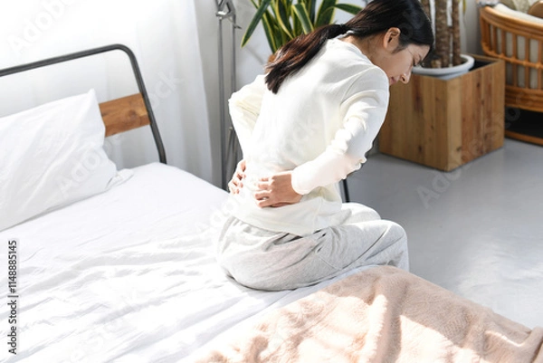 Fototapeta ベッドの上で腰痛や背痛に悩むアジア人女性