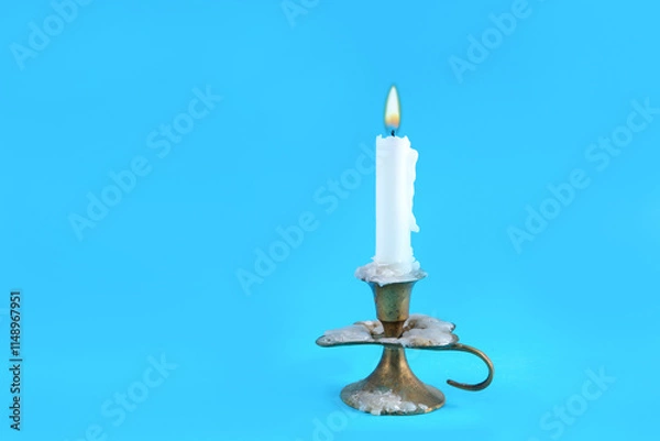 Obraz Very old retro candle in a candlestick with a burning flame on a classic blue background in a studio. Fire and minimalism concept with copy space for text or design