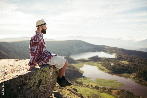 Fototapeta Man sitted in a rock looking at the lake in the mountains