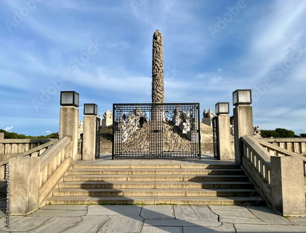 Fototapeta The entrance to Monolitten in Vigeland Park, Oslo, featuring a majestic wrought-iron gate with intricate designs, leading to the iconic sculpture surrounded by greenery.
