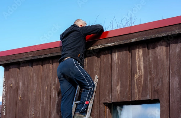 Fototapeta A man climbs the stairs on the roof of a small country house