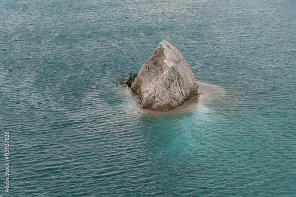 Fototapeta A quarry with blue or turquoise water and a small rocky island, slight waves on the water. Chalk deposits