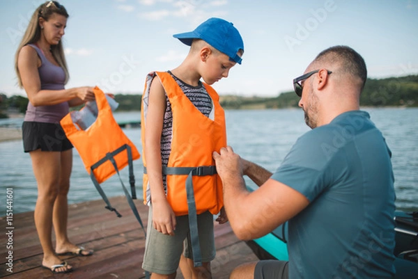 Fototapeta Father helping his son put on a life jacket before kayaking