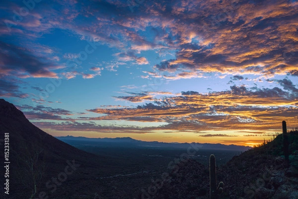 Fototapeta Sunset creating vibrant cloud formations over a desert landscape, showcasing natural beauty and tranquility. Captured with hills, cacti, and expansive horizons, providing a stunning and peaceful view.
