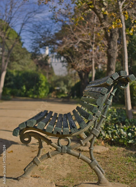 Obraz A classic park bench with a backdrop of trees and greenery. The framing highlights the blend of rustic architecture with the serenity of nature, evoking nostalgia and relaxation. 