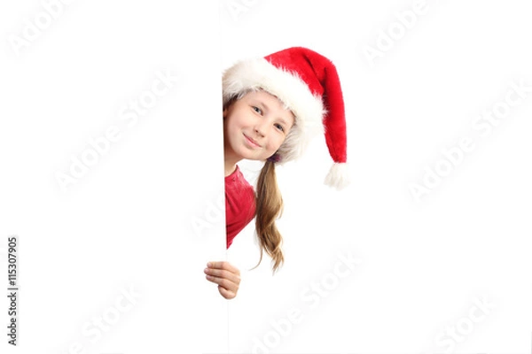 Fototapeta the portrait of smiling little girl on Santa Claus hat peeking by the white board looking at camera isolated on white background.