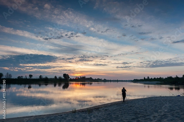 Fototapeta Matins landscape on a wide river. Summer. Sunrise. Photographer and tripod. Sandy beach. Reflection of clouds in the water