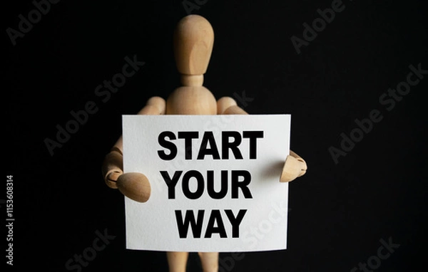 Fototapeta The wooden man holds a white sign with the text START YOUR WAY in his hands. The content of the lettering has implications for business concept and marketing.