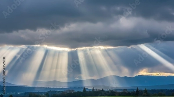 Fototapeta Dramatic sun rays breaking through dark clouds over mountains.