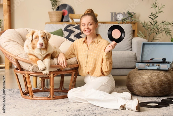 Obraz Young woman with vinyl disk for record player and Australian Shepherd dog on armchair at home
