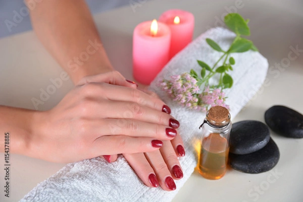 Fototapeta Female hands with red nail polish on a towel in a beauty studio on a white desk with decorations. Manicure and beauty concept