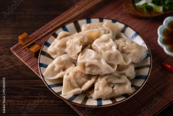 Fototapeta Eating fresh boiled dumpling using chopsticks with soy sauce.